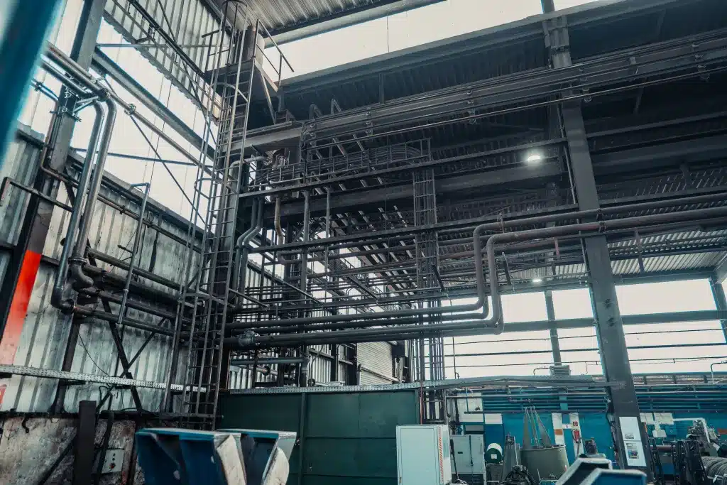 Eine große Industriehalle im Stahlbau. Man sieht etliche auf mehreren Metern Höhe angebrachte Verrohrungen Leitern und Kabel. Das Ergebnis von gutem Rohrleitungsbau