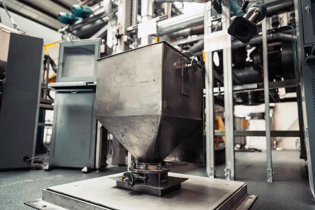 Stahlbau 8 Ein großer Stahltrichter mit einem Gewinde zum Öffnen und Schließen der Lucke am unteren Ende. Der Behälter ist an eine große, am Boden montierte Stahlplatte montiert.