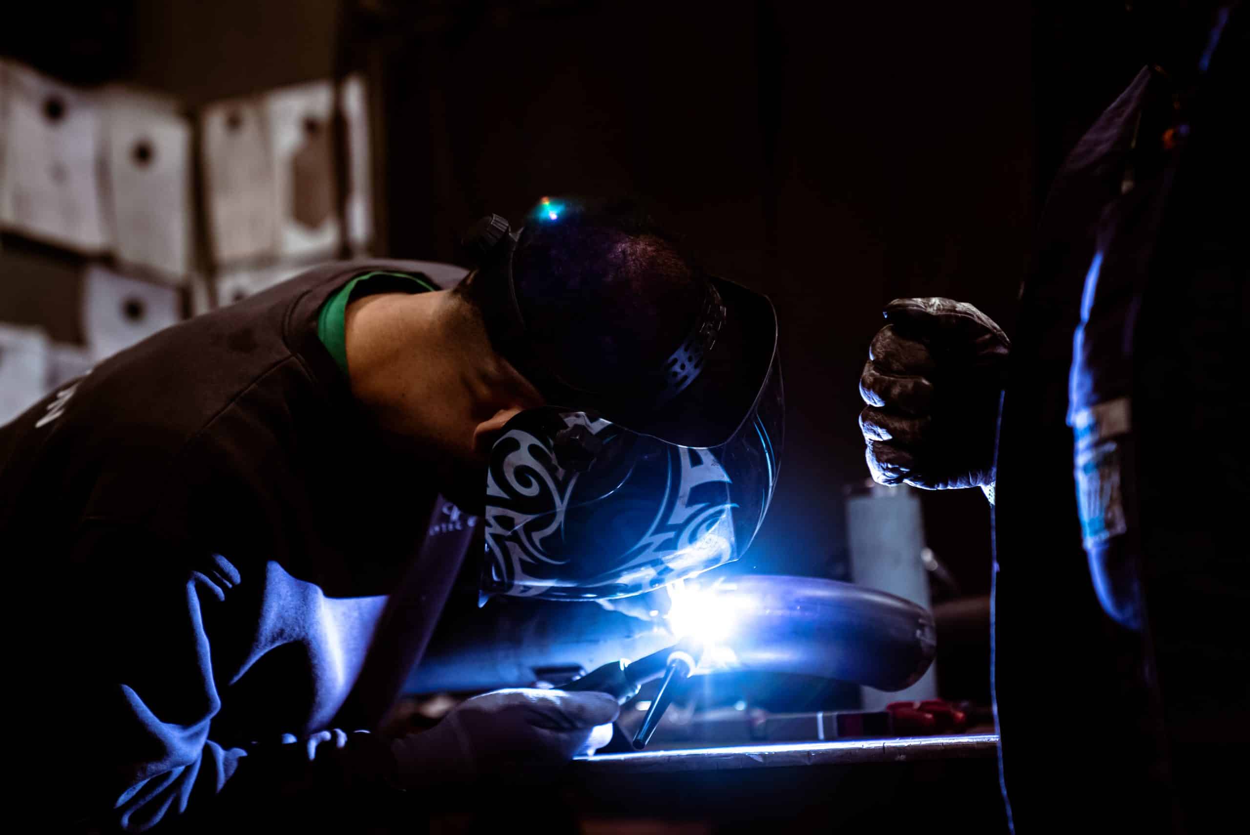 Ein mann schweißt ein Stück Stahlrohl an ein anderes Rohr, dies wird für die Heißwasserleitungen einer Kesselanlage genutzt. Dies bezeichnet man auch als Rohrleitungsbau