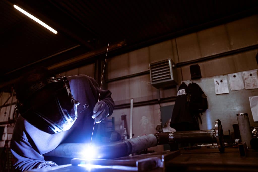 Schweißtechnik 6 Ein mann schweißt ein Stück Stahlrohl an ein anderes Rohr, dies wird für die Heißwasserleitungen einer Kesselanlage genutzt. Dies bezeichnet man auch als Rohrleitungsbau