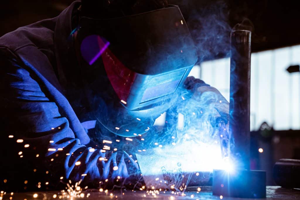 Schweißtechnik 2 Ein Mann schweißt eine Röhre auf einen Stahlring. er trägt eine Schweißerschutzmaske