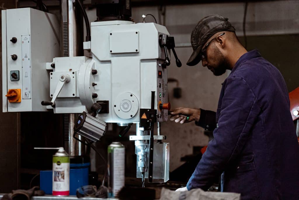 Industrieservice 6 Ein Mann steht an einem Standbohrer und bohrt ein Loch in eine Stahlplatte