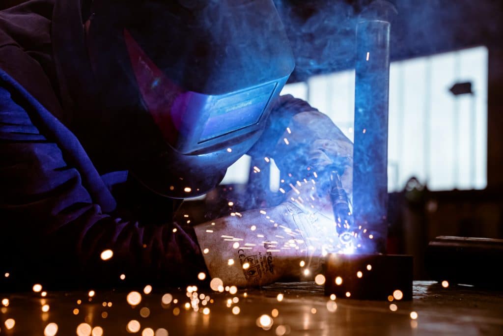 Industrieservice 7 Ein Mann schweißt eine Röhre auf einen Stahlring. er trägt eine Schweißerschutzmaske