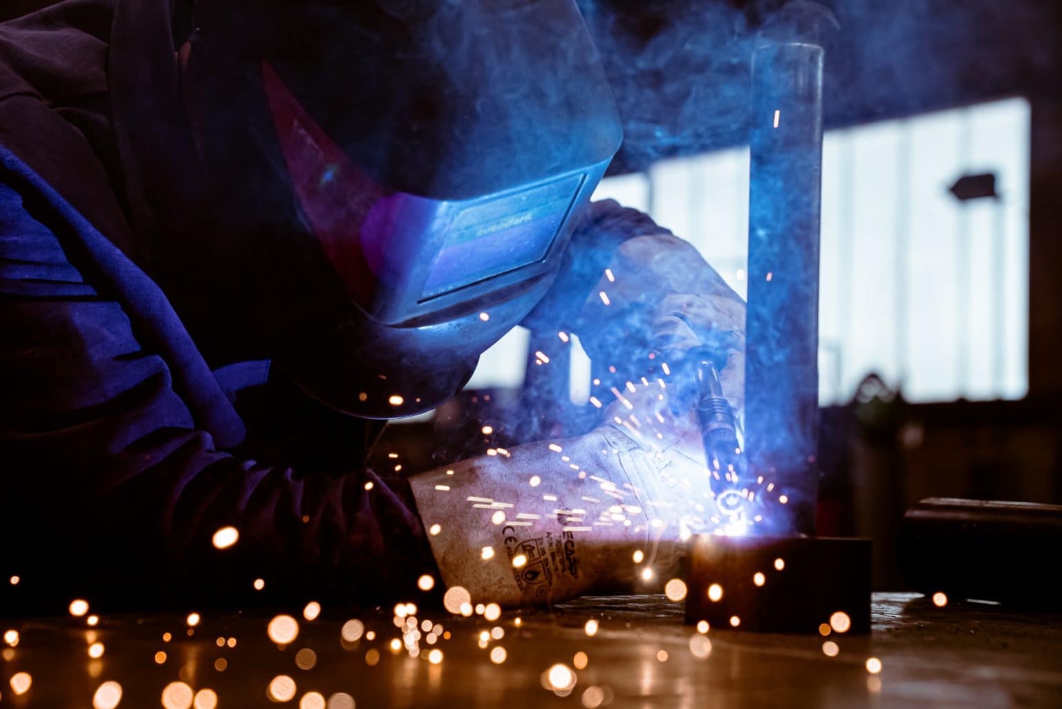 Ein Mann schweißt eine Röhre auf einen Stahlring. er trägt eine Schweißerschutzmaske