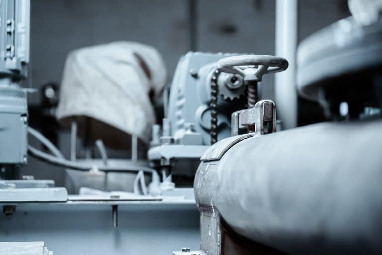 Röhre in einem Industriebetrieb, es gibt Stellschrauben und Stellmotoren, die über Zahnräder und Ketten angetrieben werden